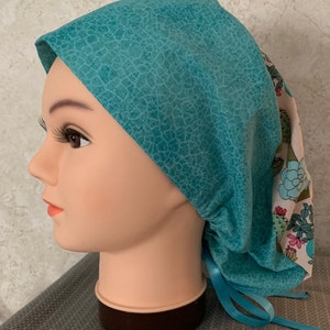 May include: A turquoise scrub hat with a white and pink cactus print. The hat has a tie at the back.