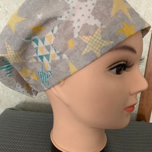 May include: Grey scrub hat with a pattern of yellow and teal stars. The stars have different patterns, including polka dots, stripes and geometric shapes.