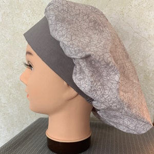 May include: A grey and white patterned scrub hat with a grey band around the bottom. The hat is made of soft, comfortable fabric and is ideal for keeping hair out of the way while working.