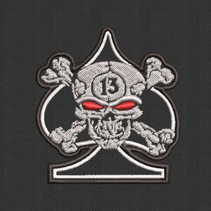 May include: A silver skull with red eyes and crossed bones is embroidered on a black background. The skull has the number "13" on its forehead. The skull is inside a white outline of a spade.