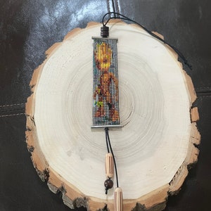 May include: A beaded bracelet with a colorful image of a character from the Guardians of the Galaxy movie. The bracelet has a brown leather cord and wooden beads.