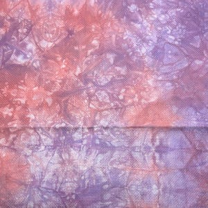May include: Close-up of a fabric with a tie-dye pattern in shades of pink, purple, and white. The fabric has a textured weave, with the colours blending together in a soft, watercolour-like effect. The overall look is artistic and unique.