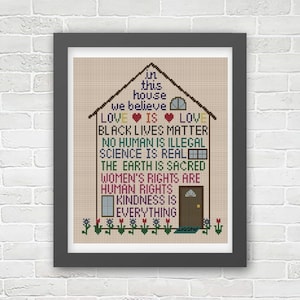 K&ouml;nnte beinhalten: Ein Kreuzstich-Design eines Hauses mit dem Text "In diesem Haus glauben wir: Liebe ist Liebe, Black Lives Matter, Kein Mensch ist illegal, Wissenschaft ist real, Die Erde ist heilig, Frauenrechte sind Menschenrechte, Freundlichkeit ist alles."