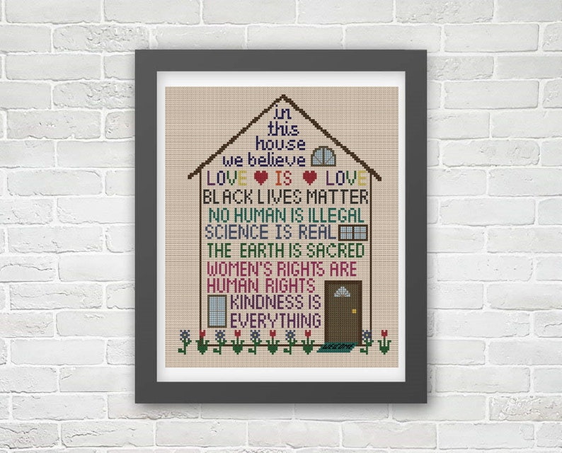 K&ouml;nnte beinhalten: Ein Kreuzstich-Design eines Hauses mit dem Text "In diesem Haus glauben wir: Liebe ist Liebe, Black Lives Matter, Kein Mensch ist illegal, Wissenschaft ist real, Die Erde ist heilig, Frauenrechte sind Menschenrechte, Freundlichkeit ist alles."
