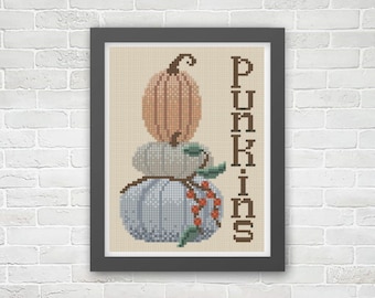 May include: Framed cross-stitch art featuring a stack of three pumpkins in shades of orange, gray, and blue. The word "Pumpkins" is stitched vertically in brown. The artwork is displayed in a black frame against a beige background.