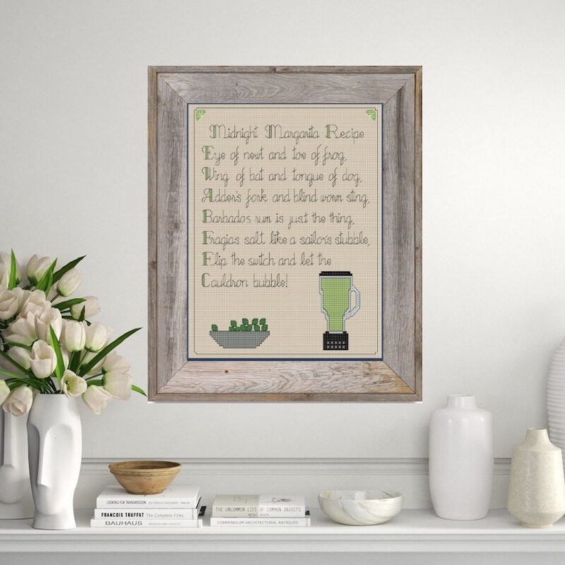 May include: A framed cross-stitch design with a recipe for a "Midnight Margarita" using ingredients like "eye of nest and toe of frog" and "wing of bat and tongue of dog". The design includes a blender and a bowl of green peas.