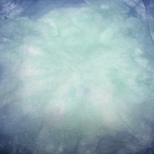 May include: A close-up of a blue and green textured fabric with a subtle gradient effect. The fabric has a woven pattern and a slightly rough texture.