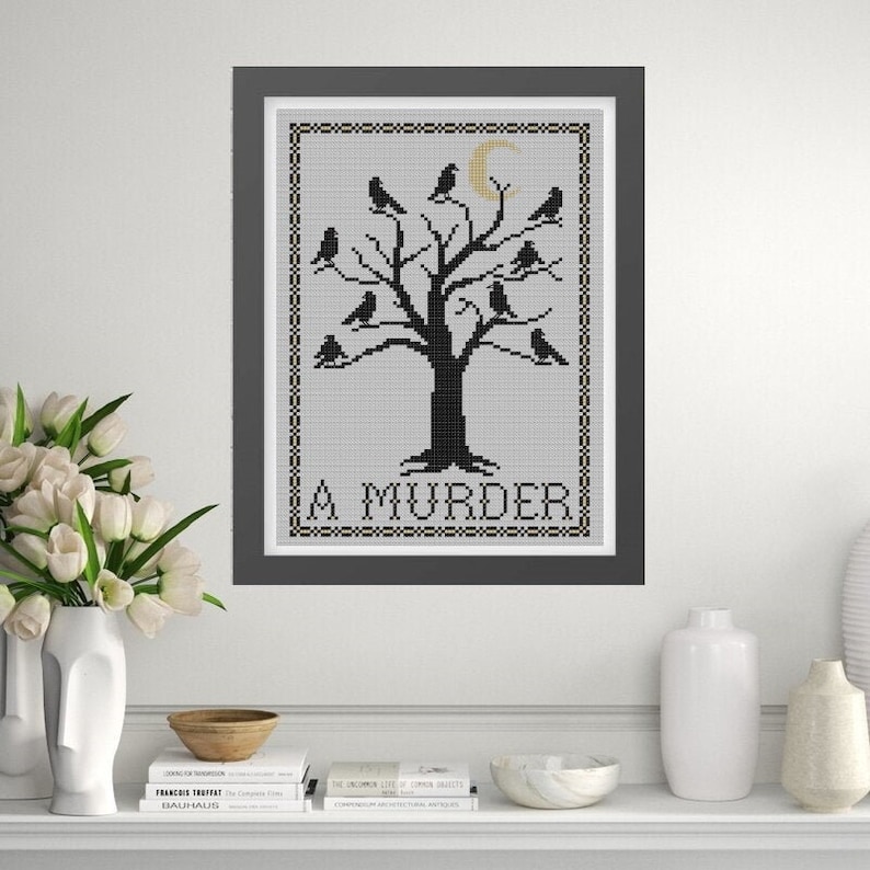 May include: Black and white cross-stitch embroidery of a tree with a crescent moon and birds, with the text "A MURDER" below the tree.