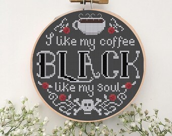 Op de afbeelding: Een borduurring met kruissteek met de tekst "I like my coffee BLACK like my soul." Het ontwerp toont een koffiekopje, bloemmotieven en een schedel. De achtergrond is donkergrijs en de ring is van hout.