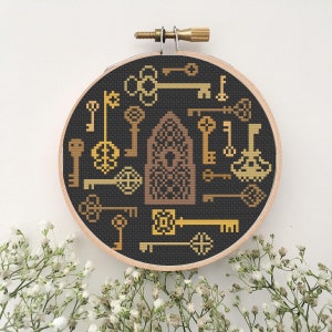 May include: A black and gold embroidery hoop with a cross-stitch design of a keyhole and many keys. The keys are in various shapes and sizes and are all gold.