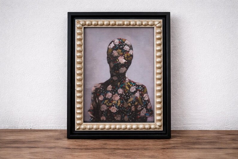 May include: Framed artwork featuring a figure with a floral pattern covering the head and upper body. The artwork is in a black frame with a gold beaded inner border. The background is a light gray color.