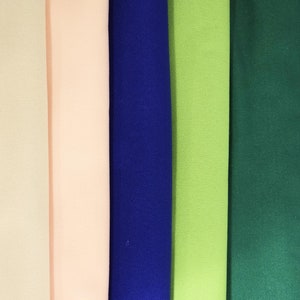 May include: A vertical arrangement of fabric swatches in various colors. The colors include cream, light pink, royal blue, lime green, forest green, white, and black. The fabric appears to be a solid color, possibly cotton or a similar material.