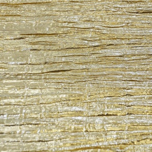 May include: Close-up of a textured fabric with a metallic gold and silver sheen. The fabric has a crinkled appearance, with horizontal lines and subtle variations in color and texture, creating a luxurious look.