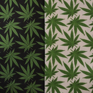 May include: A fabric with a repeating pattern of green marijuana leaves on a black background on the left side and a white background on the right side.