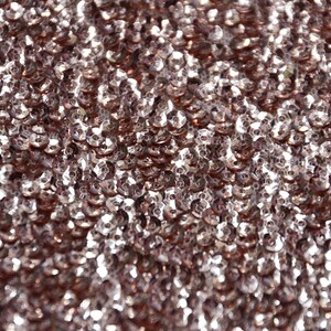 Puede incluir: Primer plano de una tela de color oro rosa con una superficie texturizada hecha de pequeñas lentejuelas redondas.