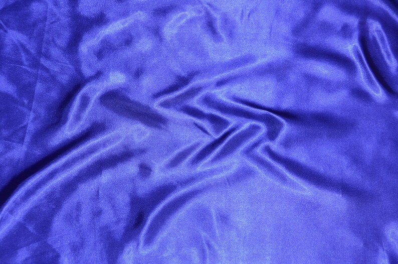 May include: A close-up of a smooth, blue satin fabric with soft folds and wrinkles.