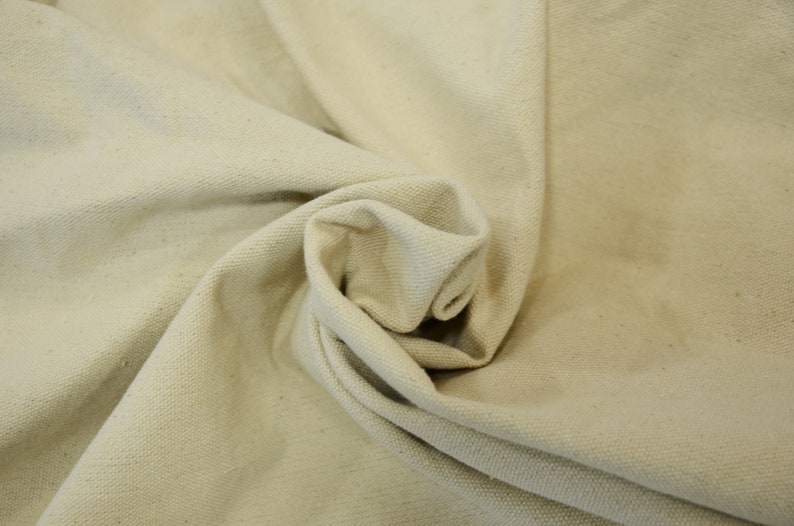 May include: Close-up of a natural off-white canvas fabric with a textured weave. The fabric is folded and draped, showing its soft and pliable texture.
