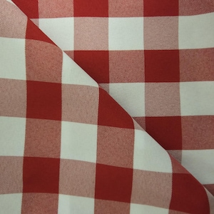 May include: Red and white checkered fabric with a diagonal fold. The fabric has a woven texture.