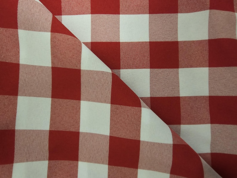 May include: Red and white checkered fabric with a diagonal fold. The fabric has a woven texture.