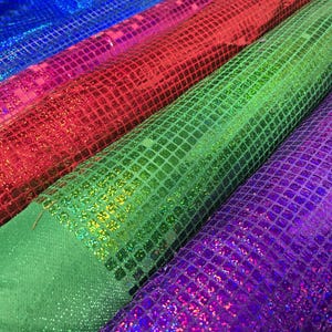 May include: Four rolls of iridescent fabric with a square pattern. The fabric is blue, red, green, and purple.