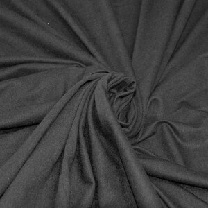 May include: A close-up of a dark gray fabric with a soft, smooth texture. The fabric is draped and folded, creating a swirling pattern.