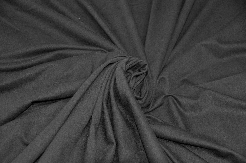 May include: A close-up of a dark gray fabric with a soft, smooth texture. The fabric is draped and folded, creating a swirling pattern.