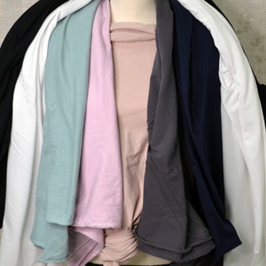 May include: A stack of seven t-shirts in various colors, including black, white, light blue, pink, gray, and navy blue.