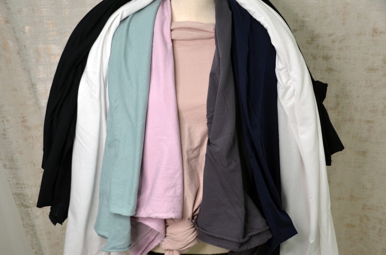 May include: A stack of seven t-shirts in various colors, including black, white, light blue, pink, gray, and navy blue.