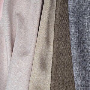May include: Close-up of various fabric swatches in shades of pink, beige, and gray. The fabrics have a textured appearance, with visible woven patterns. The colors range from light pink to a deep brown and a textured gray.