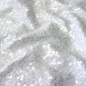 May include: White sequin fabric with a subtle shimmer. The sequins are small and closely packed together, creating a smooth and elegant texture.
