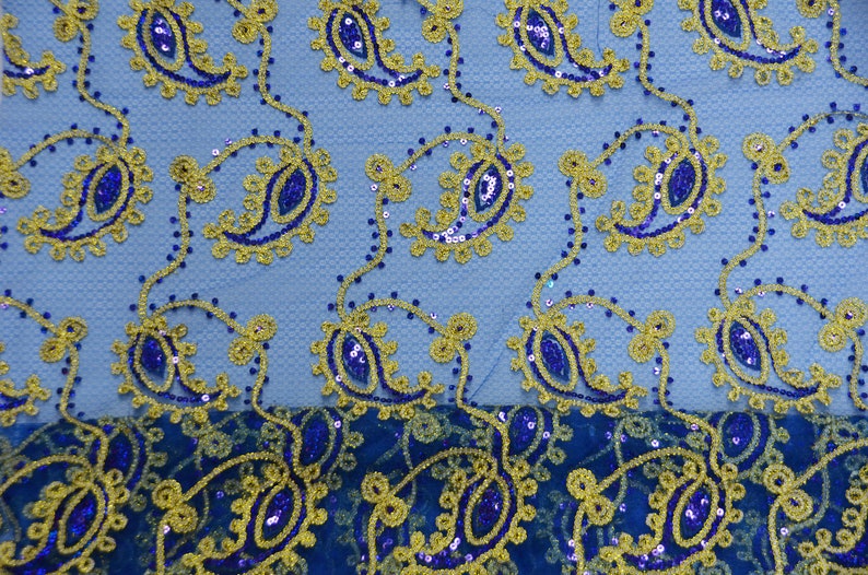 Może przedstawiać: Tkanina w wz&oacute;r paisley w kolorze niebieskim i złotym z cekinami. Tkanina ma jasnoniebieskie tło z ciemnoniebieskim wzorem paisley i złotymi akcentami.