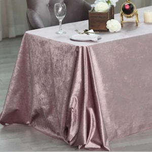 May include: A dusty rose velvet tablecloth draped over a table with a white plate, cutlery, and a glass of water. The tablecloth has a soft, luxurious feel and is perfect for adding a touch of elegance to any event.