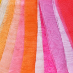May include: A collection of sheer fabric swatches in various shades of orange, pink, and red. The fabric is arranged in a rainbow pattern, with the lightest colors at the top and the darkest colors at the bottom.
