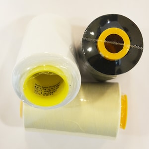 May include: Three spools of thread, one white, one black, and one beige. The spools are wrapped in clear plastic and have yellow labels. The white spool has the text "100% spun Polyester 120/2 110g 120m 120/2 made in PRC COL. WHITE 3'9999005"