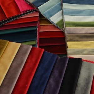 May include: A selection of fabric swatches in various colours and textures, including red, blue, green, brown, and beige. The swatches are arranged in a fan shape, with the edges of the fabric overlapping.