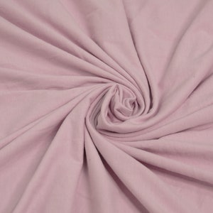 May include: A close-up of a soft, pale pink fabric with a smooth texture. The fabric is folded and draped, creating a swirling pattern.