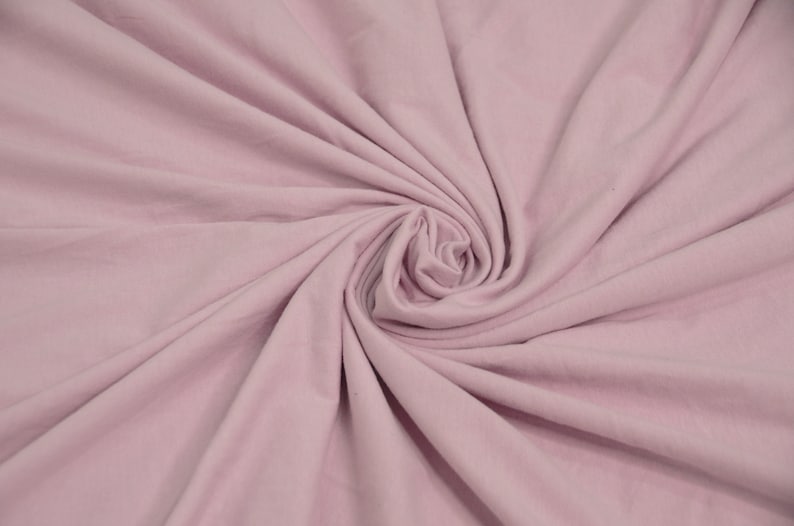 May include: A close-up of a soft, pale pink fabric with a smooth texture. The fabric is folded and draped, creating a swirling pattern.