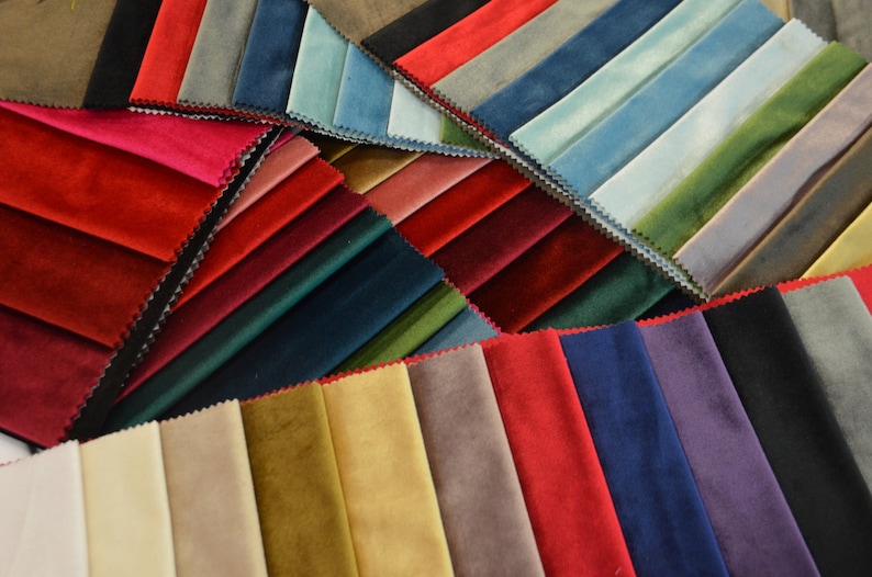 May include: A collection of fabric swatches in various colours, including red, green, blue, and beige. The swatches are arranged in a fan shape, showcasing the different textures and shades.