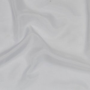 Peut inclure: Tissu blanc avec une texture lisse et soyeuse. Le tissu est drapé et plié, créant des lignes douces et fluides.