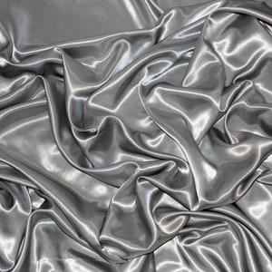 May include: A close-up of a silver satin fabric with soft, flowing folds and a smooth, luxurious texture.