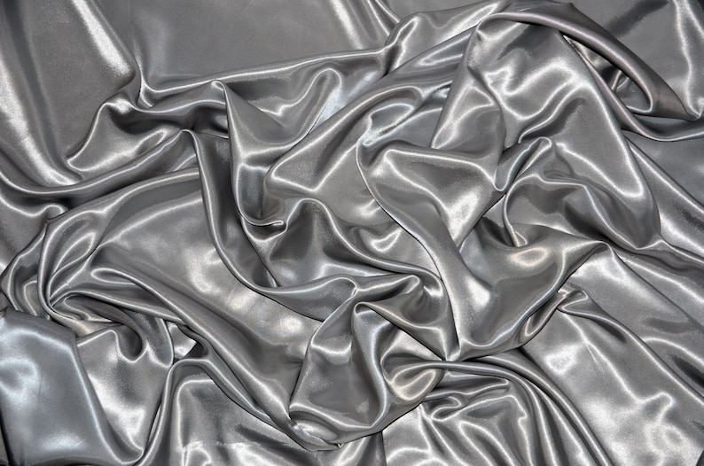 May include: A close-up of a silver satin fabric with soft, flowing folds and a smooth, luxurious texture.