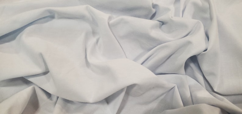 Peut inclure: Un tissu bleu clair avec une texture douce et lisse. Le tissu est pli&eacute; et drap&eacute;, cr&eacute;ant un sentiment de mouvement et de fluidit&eacute;.