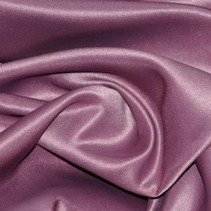 Puede incluir: Primer plano de una tela suave, lisa y malva con un brillo sutil. La tela est&aacute; drapeada y doblada, creando una textura lujosa y elegante.