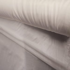 Puede incluir: Tela blanca con una textura lisa. La tela est&aacute; doblada y enrollada, mostrando los bordes.
