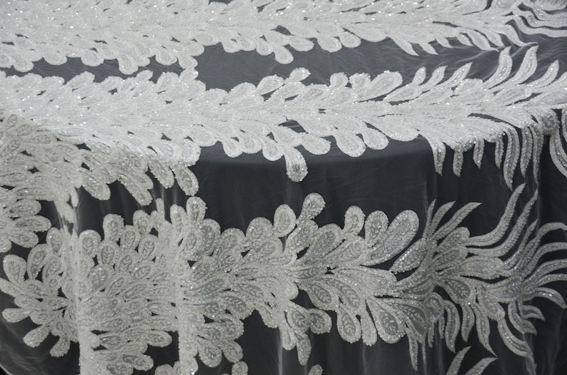 Puede incluir: Camino de mesa blanco con cuentas con un delicado dise&ntilde;o floral. El camino de mesa est&aacute; hecho de una tela transparente con un brillo sutil.