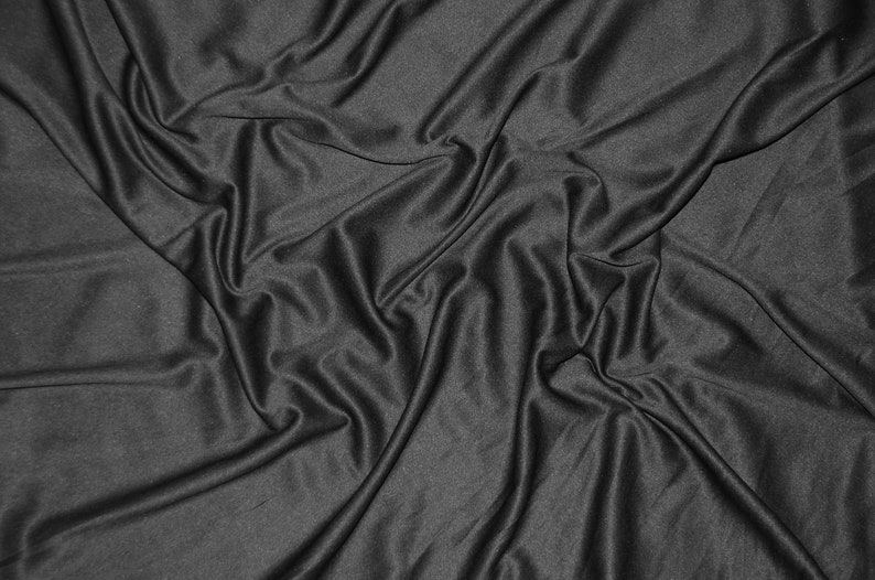 Puede incluir: Primer plano de una tela suave y negra con pliegues y arrugas suaves. La tela est&aacute; drapeada y texturizada, creando un aspecto dram&aacute;tico y elegante.