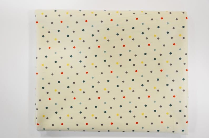 May include: Cream-colored fabric with a repeating pattern of small, colorful polka dots. The dots are in shades of red, yellow, green, and gray.