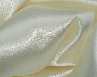 May include: Close-up of a smooth, ivory-colored satin fabric with a subtle sheen. The fabric is folded and draped, showcasing its luxurious texture.