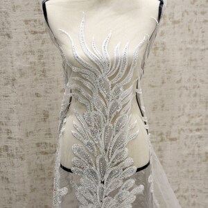 Puede incluir: Tela de encaje blanca con cuentas con un dise&ntilde;o floral. La tela est&aacute; en un maniqu&iacute; blanco.