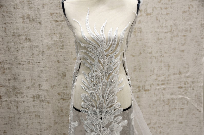 Puede incluir: Tela de encaje blanca con cuentas con un dise&ntilde;o floral. La tela est&aacute; en un maniqu&iacute; blanco.